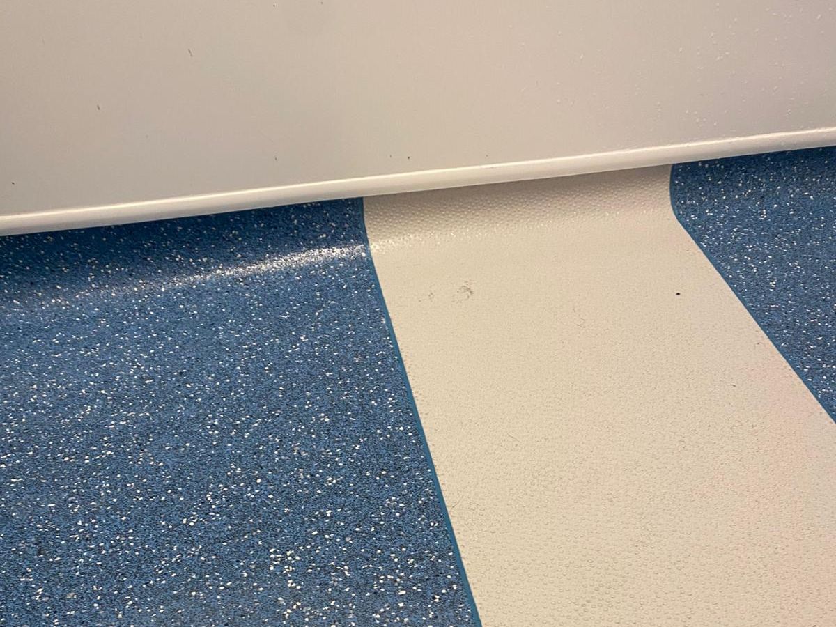 Close-up of blue speckled and cream vinyl turned up the wall to form a coved skirting edge