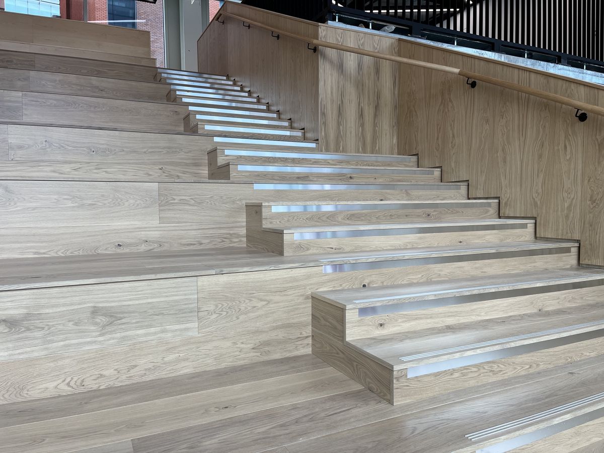 Tiered oak hardwood stairs with aluminium stair nosings, beside oak-clad walls and a handrail